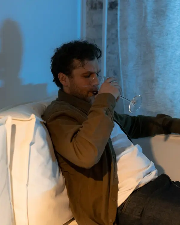 Homem bebendo sozinho no sofá, à noite