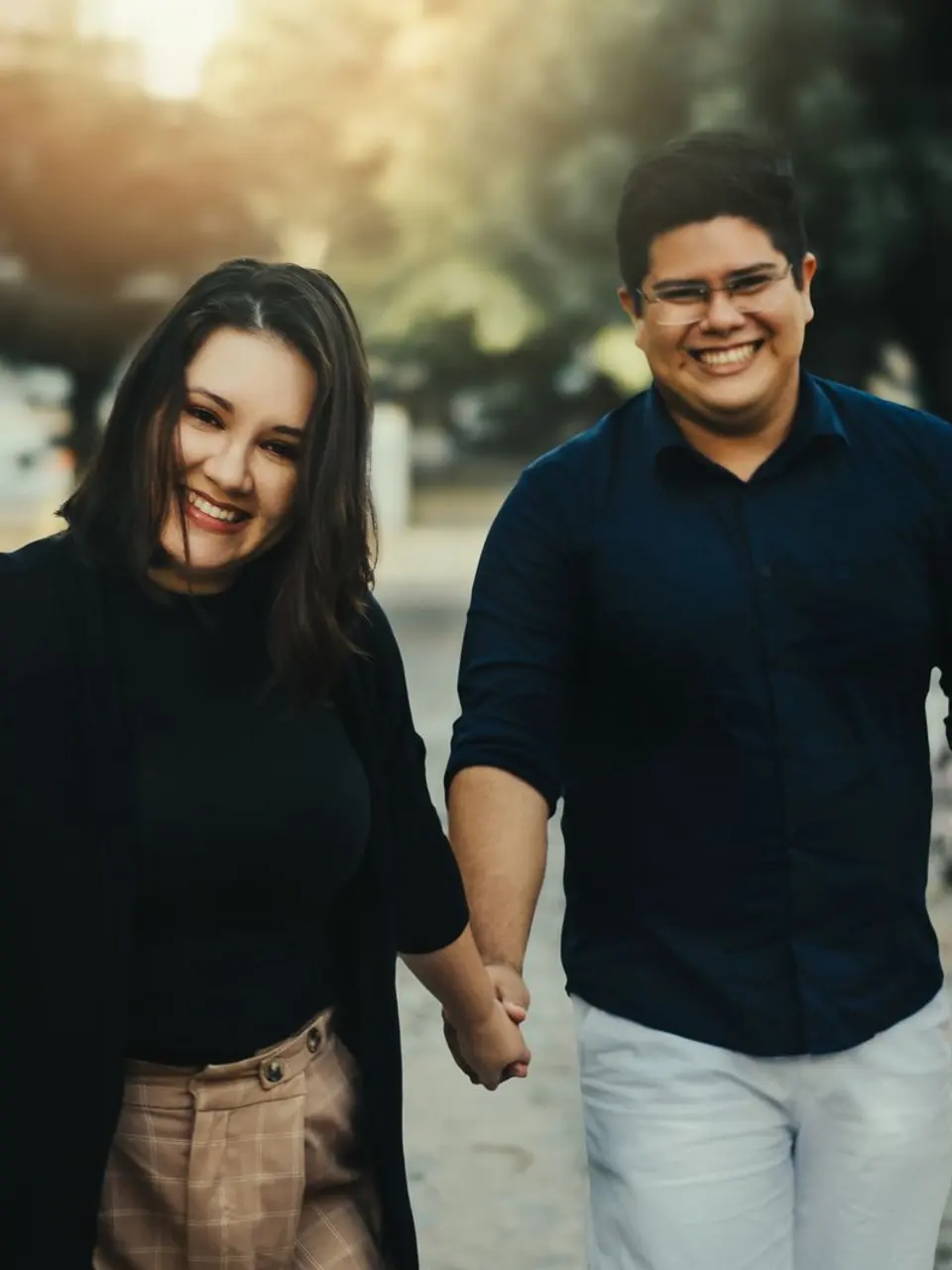 Casal sorrindo, de mãos dadas, caminhando junto